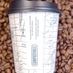 Photo of compostable coffee cup on a background of coffee beans.